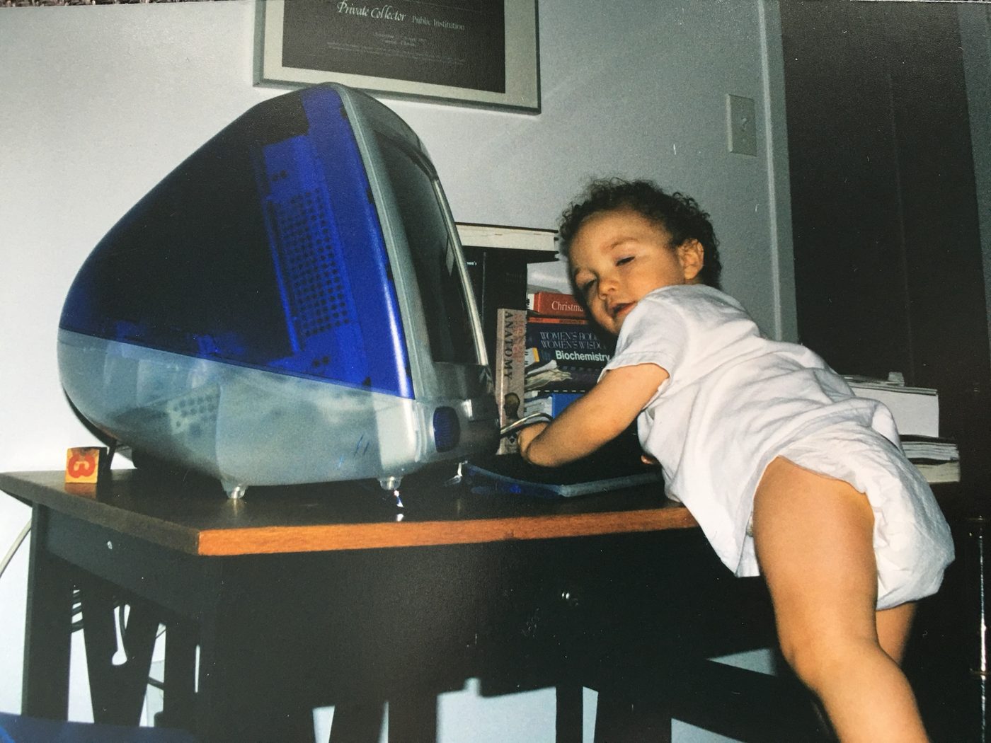 Alex as a toddler in a diaper, reaching across a desk to the keyboard of a blue iMac